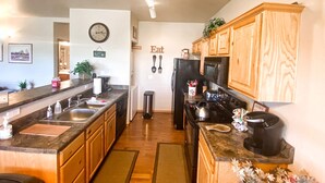 A modern kitchen with wooden cabinets, a black refrigerator, a stove, and a microwave. There is a sink with a faucet, a countertop with various items, and a clock on the wall. - Gorgeous 2BR/2BA with Stunning Views and Great Location (Show Low)