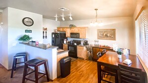 A compact kitchen with wooden cabinets, a refrigerator, a microwave, and a dining area with a table and chairs. - Gorgeous 2BR/2BA with Stunning Views and Great Location (Show Low)