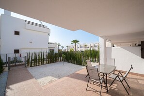 A patio with a glass table and chairs, surrounded by a gravel area and a low fence.