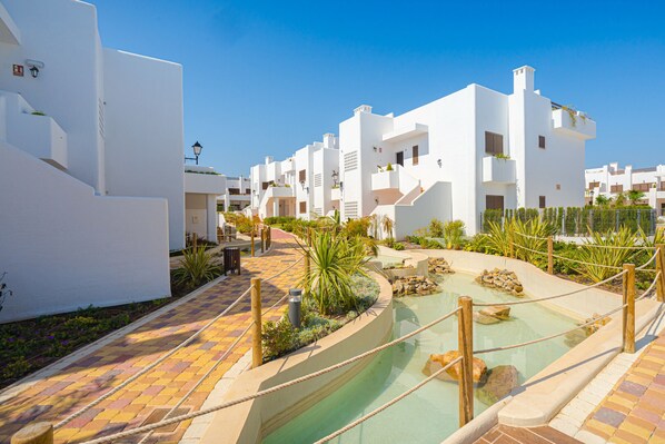 A resort with white buildings, a pool area, and a paved walkway.