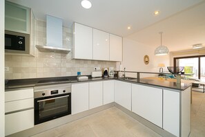A modern kitchen with white cabinetry, a built-in oven, a microwave, and a coffee maker.