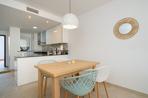 A modern kitchen with a central island, white chairs, and a wooden dining table.
