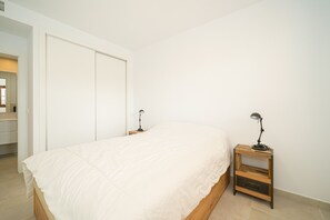 A bedroom with a bed, a wooden nightstand, and a desk lamp.
