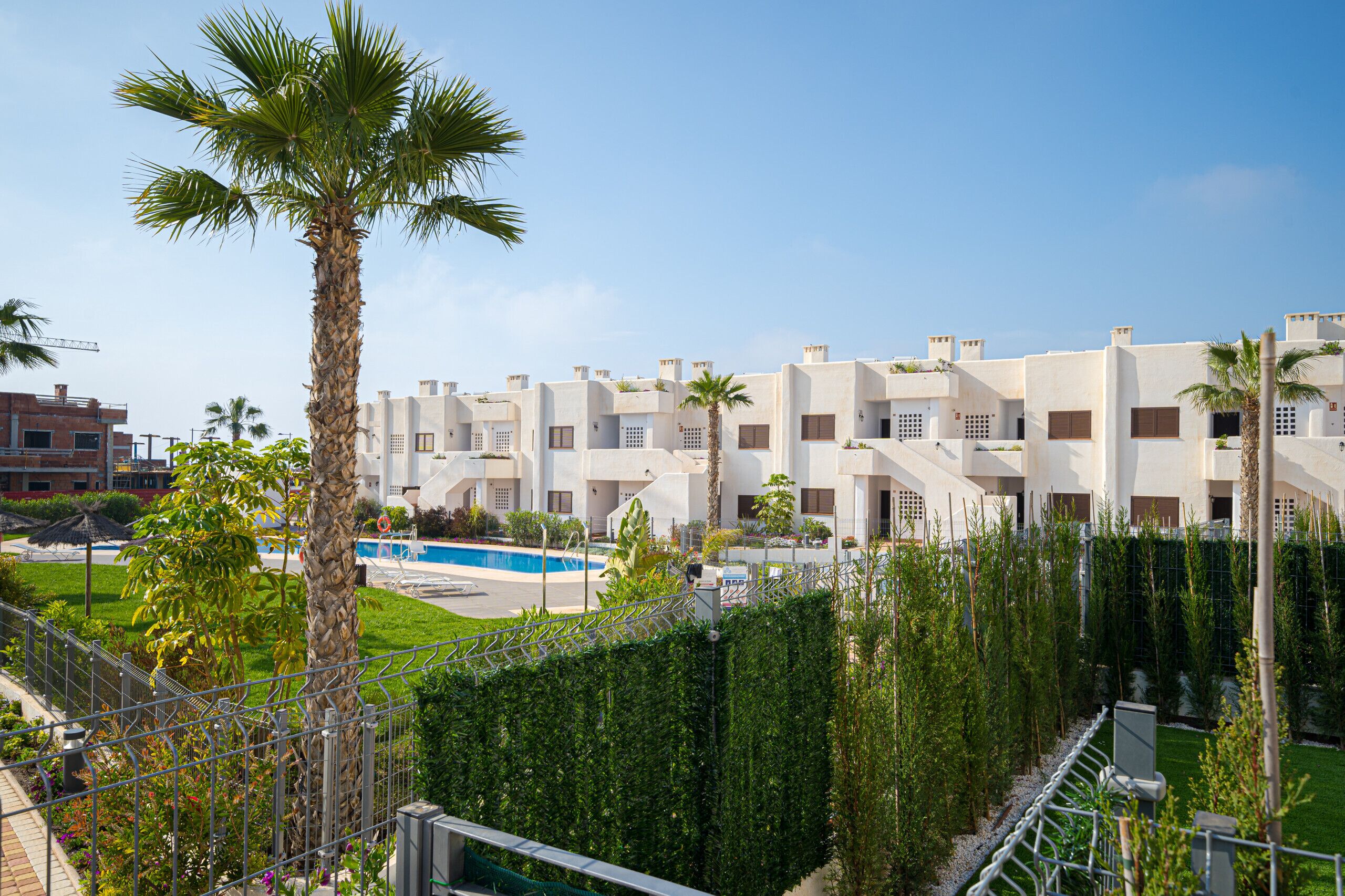 A modern residential building with a pool, palm trees, and a well-maintained garden.