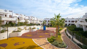 A modern residential area with white buildings, a playground, and a paved walkway. - Apartamento Babilonia (Mar de Pulpi) (San Juan de los terreros)