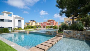 A swimming pool with stone steps and a stone wall, surrounded by a well-maintained lawn and trees. - Apartamento Balcones de la Laguna (Torrevieja)