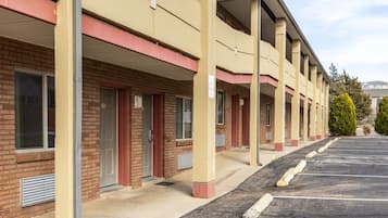 A motel with a row of rooms, a parking lot, and a clear sky.