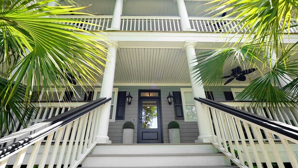 A staircase with white railings and a dark door, leading to a balcony with a ceiling fan. - High-End Beach Home, Walking Distance to Beach & Close To Town - On The Half Shell! (Folly Beach)