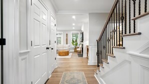 A hallway with white doors, a wooden floor, a blue rug, and a staircase with black railings. - High-End Beach Home, Walking Distance to Beach & Close To Town - On The Half Shell! (Folly Beach)