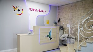Uma receção com acabamento em madeira, um relógio fixado na parede e um letreiro com a inscrição "COLIBRI".