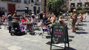 Um café ao ar livre com mesas e cadeiras, um letreiro anunciando 'Café Atlantic - A Melhor Sangria da Cidade' e vista dos edifícios ao redor.