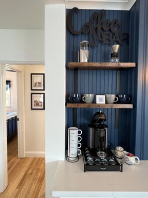 A kitchen with a coffee bar, including shelves with mugs, a coffee maker, and a coffee grinder.