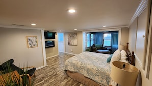 Habitación de hotel con una cama grande, televisor montado en la pared, una silla y una ventana con cortinas.