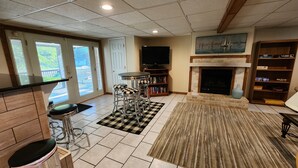 Una sala de estar con chimenea, televisor, estantería y comedor con taburetes de bar.