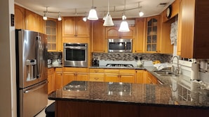 Una cocina moderna con armarios de madera, electrodomésticos de acero inoxidable, encimeras de granito e iluminación colgante.