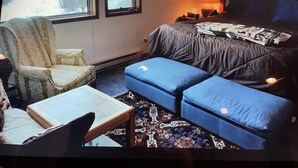 Una habitación acogedora con una cama, una silla, una mesita y una ventana que ofrece vistas a un paisaje nevado.