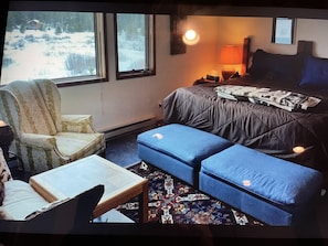 Une pièce confortable avec un lit, une chaise, une petite table et une fenêtre donnant sur un paysage enneigé.