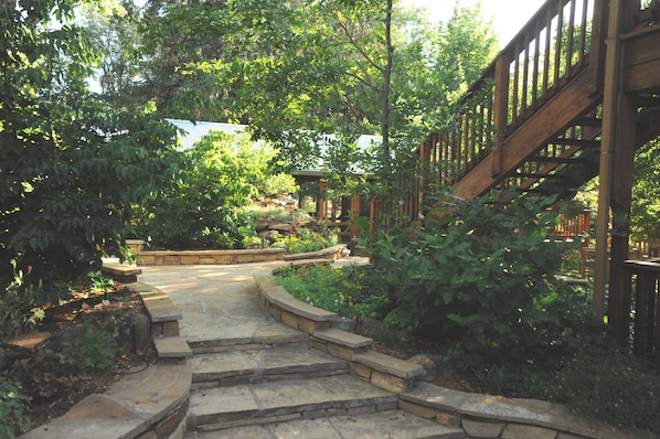 A stone staircase leading to a wooden deck surrounded by lush greenery and a small building.