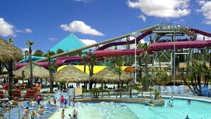 Un parc aquatique doté d’une grande piscine, de toboggans et de parasols en chaume.