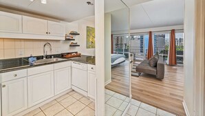Eine moderne Küche mit weißen Schränken, einer schwarzen Arbeitsplatte und einem eingebauten Ofen. Es gibt einen Essbereich mit einer Couch und Blick auf die Stadt durch große Fenster.