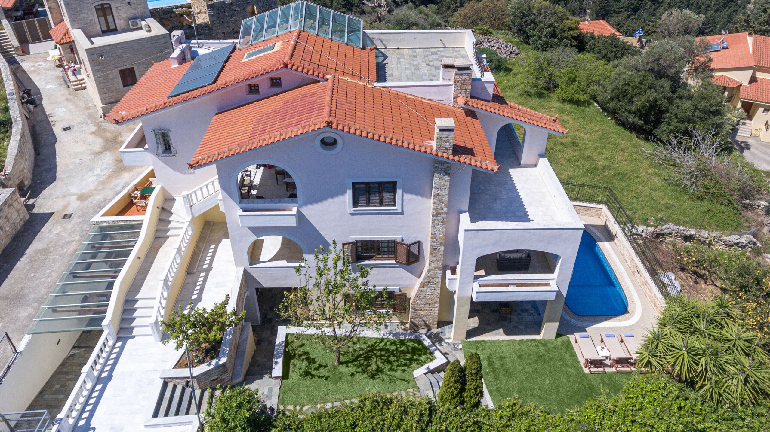 En stor, moderne villa med rødt tegltag, flere balkoner og en swimmingpool.