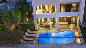 Ein zweistöckiges Haus mit Swimmingpool, Sitzgelegenheiten im Freien und einem gepflegten Garten.