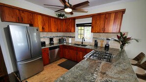 A modern kitchen with wooden cabinets, stainless steel appliances, granite countertops, and a ceiling fan. - Sunset and Ocean views at Sandy Feet Retreat with private infinity pool. (Sandy Bay)