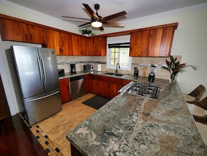 A modern kitchen with wooden cabinets, stainless steel appliances, granite countertops, and a ceiling fan. - Sunset and Ocean views at Sandy Feet Retreat with private infinity pool. (Sandy Bay)