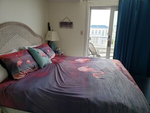 Une chambre à coucher avec un lit, des oreillers, une lampe, un élément de décoration murale et une vue sur un immeuble par la fenêtre.