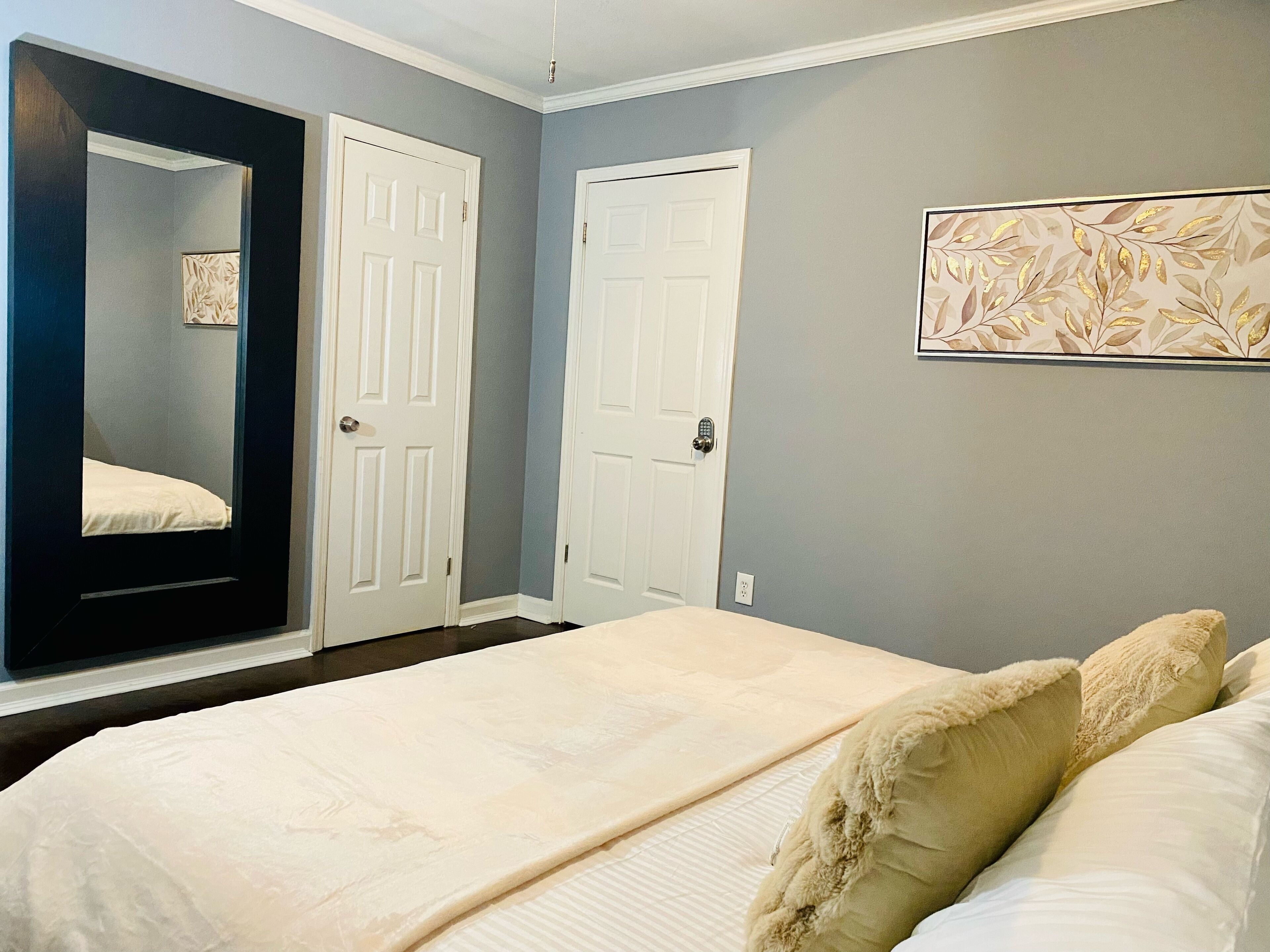A bedroom with a bed, two white doors, and a framed artwork on the wall.