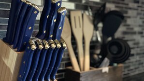 Un ensemble de couteaux à manches bleues, rangés dans un bloc en bois, devant un mur recouvert de carreaux.