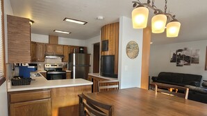 A modern kitchen with wooden cabinets, a stainless steel refrigerator, and a dining area with a wooden table and chairs. - Cozy centrally located two-bedroom home. Pet friendly!  (Fairbanks)