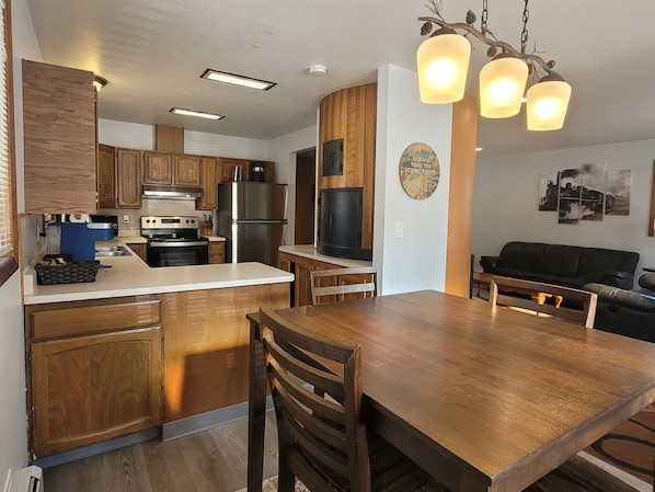 Une cuisine moderne avec des meubles en bois, un réfrigérateur en acier inoxydable et un coin repas comprenant une table et des chaises en bois.