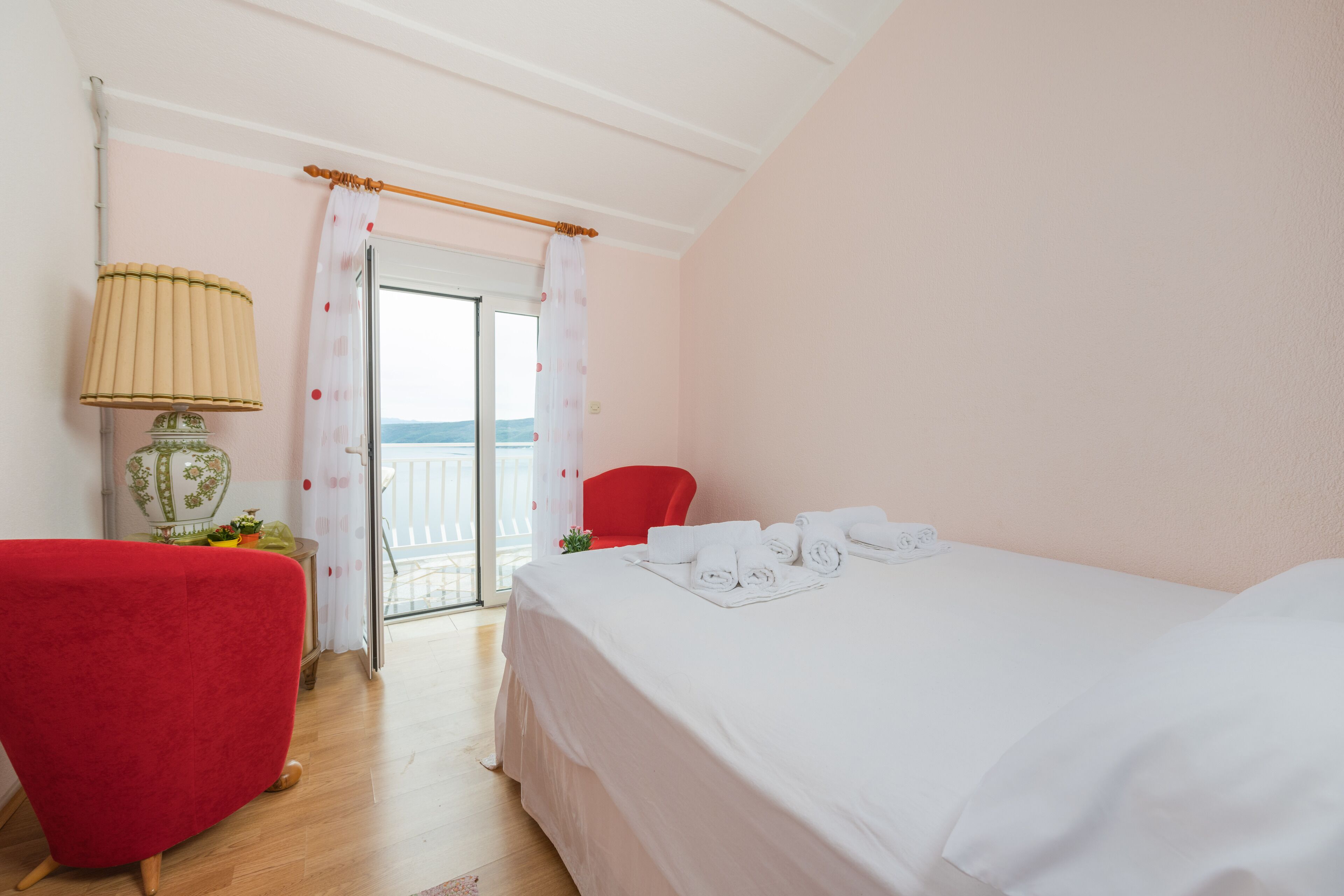 Une chambre d’hôtel avec un lit, une chaise rouge, une lampe et une vue sur l’extérieur.