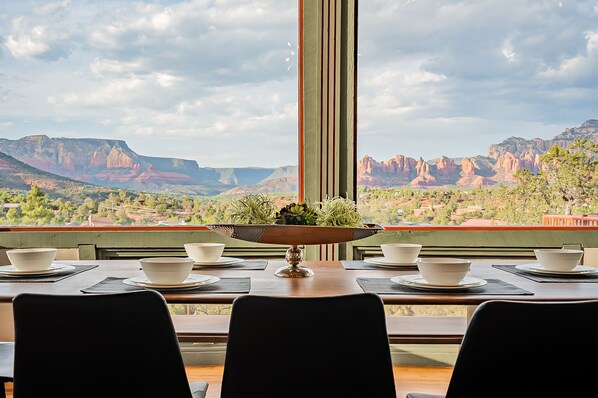 Una mesa de comedor con cuencos blancos y un cuenco decorativo, frente a un paisaje montañoso.