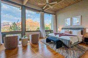 Un dormitorio con un ventanal grande, suelo de madera y una cama con almohadas y una colcha.