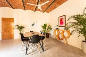 A dining area with a wooden table, black chairs, potted plants, a ceiling fan, and a wooden door.