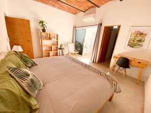 A bedroom with a large bed, a desk, a chair, a bookshelf, and a window with curtains.