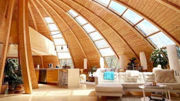 A spacious interior with a high, wooden ceiling and skylights, a kitchen area, and a living room with seating. - Unique Dome Home With Hot Tub & Piano, on 28 acres (New Paltz)