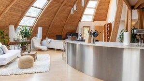 A spacious loft with a high ceiling, skylights, a kitchen area, and modern furnishings. - Unique Dome Home With Hot Tub & Piano, on 28 acres (New Paltz)