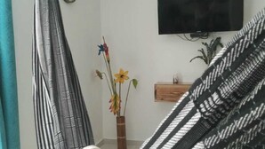 Ein Hängesessel, eine Uhr, ein Flachbildfernseher, ein Holzregal und eine Vase mit Blumen.