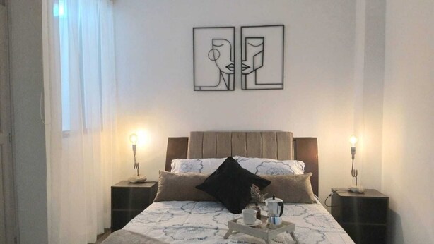 Ein Schlafzimmer mit einem Bett, zwei Nachttischen, einer Nachttischlampe, einem Couchtisch mit Tasse und Kanne sowie zwei Wandbildern.