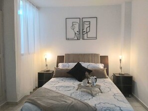 Una camera da letto con un letto, due comodini, una lampada da comodino, un tavolino da caffè con una tazza e una caffettiera, e due opere d'arte appese alle pareti.