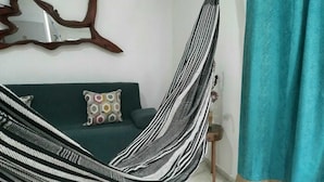 Ein Hängestuhl in einem Wohnzimmer mit einem grünen Sofa und gemusterten Kissen.