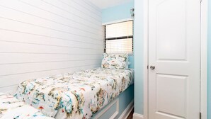Une petite chambre avec un lit simple, une fenêtre avec des stores et une porte blanche.