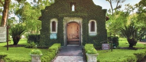 Una pequeña iglesia con un camino de piedra que lleva a la entrada, rodeada de follaje cuidado y un cielo despejado.