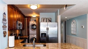 Une cuisine dotée de plans de travail en granit, d’appareils électroménagers en acier inoxydable, d’armoires en bois et d’un lave-linge et d’un sèche-linge intégrés.