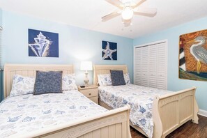 A bedroom with two beds, a ceiling fan, and artwork on the walls. - Seaside Sunrise (St Augustine)