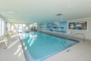 An indoor swimming pool with clear water, a mural of dolphins on the wall, and a view of the outside through large windows. - Seaside Sunrise (St Augustine)