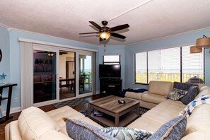 A living room with a ceiling fan, a television, a sofa, and a coffee table. - Seaside Sunrise (St Augustine)